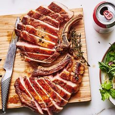 sliced meat on cutting board next to salad and can of soda with utensils