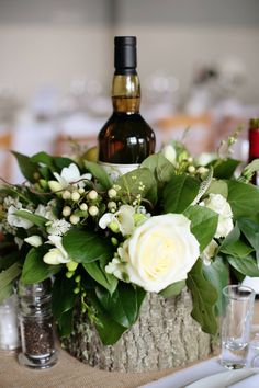 a table topped with a vase filled with white flowers and greenery next to a bottle of wine