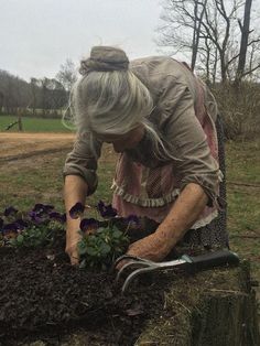 an older woman is digging in the ground with flowers and gardening utensils on her knees