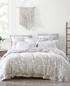 a bed with white comforter and pillows in a room next to a plant on the floor