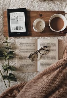 an open book, cup of coffee and reading glasses on a bed next to a tablet