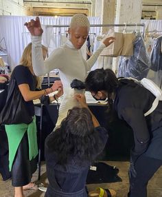 three women working on clothing in a room with clothes hanging from the rack and another woman looking down