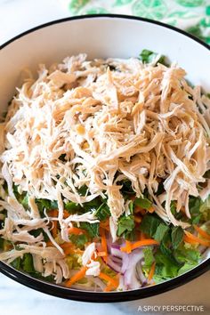 a salad with shredded cheese and vegetables in a black bowl on a white tablecloth