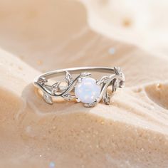 a white opal ring sitting on top of sand