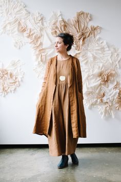 a woman standing in front of a wall with paper flowers on it and a coat over her shoulders