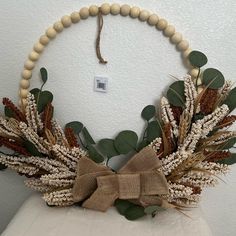 a wreath made out of fake plants and burlocks on a white chair with a brown bow