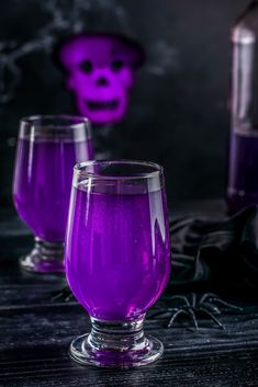 two purple wine glasses sitting next to each other on a table with a skull in the background