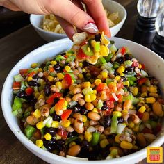 a person scooping corn into a white bowl filled with beans and veggies