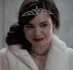 a woman with a tiara on her head and red lipstick in front of the camera