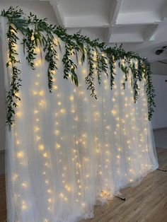 the curtain is covered with lights and greenery hanging from it's sides in front of a wooden floor