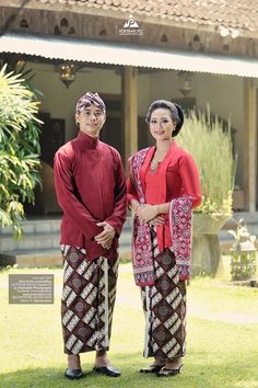 two people standing next to each other in front of a building with grass and trees