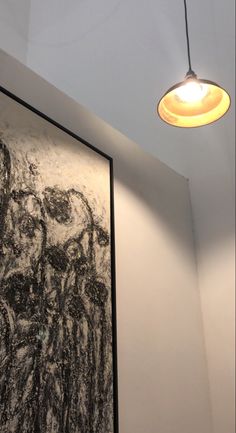 a light hanging from the ceiling in a room with paintings on the wall and below it