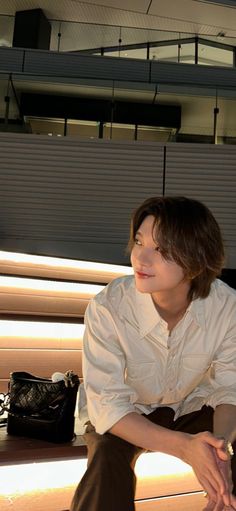 a young man sitting on top of a wooden bench next to a black handbag