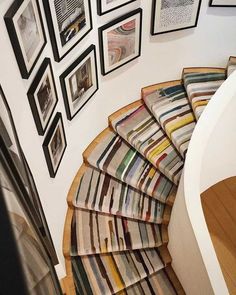 a spiral staircase with pictures on the wall and rugs hanging up against it's sides