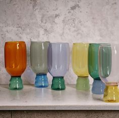 there are many different colored glass cups on the counter top, all lined up and ready to be used