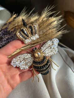 two brooches in the shape of bees with crowns on their heads are being held by someone's hand