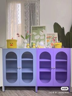 a purple and blue cabinet sitting in front of a window next to a potted plant