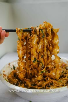 someone is eating noodles with chopsticks in a white bowl on top of a table