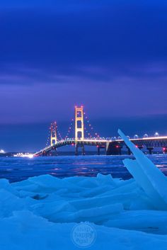 a bridge that is over some water in the snow at night with lights on it