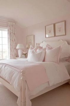 a white bed sitting in a bedroom next to a window with pink curtains and pillows