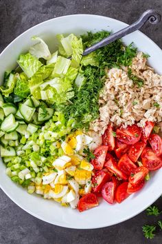 a white bowl filled with chopped vegetables and salad dressing on top of a gray surface