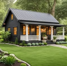 a small black house with white porches and lights on the windows is surrounded by lush green grass