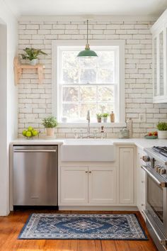 A kitchen with white exposed brick backsplash and minimalist white cabinetry. Exposed Brick Kitchen Backsplash, White Exposed Brick, White Brick Backsplash, Green Pendant Light