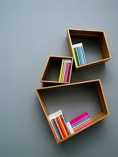 three wooden shelves with books on them against a gray wall, each holding different colored books