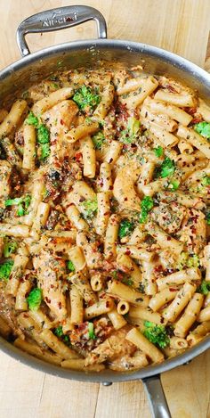 a pan filled with pasta and broccoli on top of a wooden table