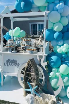 an ice cream cart decorated with blue and white balloons, cupcakes and desserts