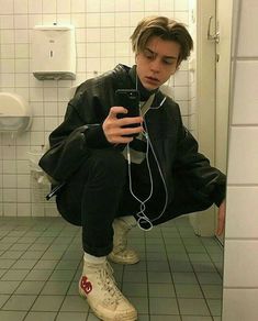 a young man squatting on the floor with headphones in his ears while looking at his cell phone