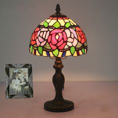 a lamp with a pink rose on it next to a picture frame