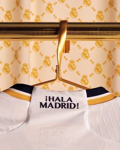 a white shirt with the word i hala madrid on it hanging from a gold hanger