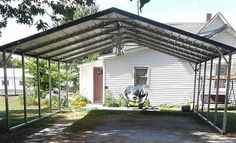 a white house with a car parked in the driveway under a metal carporture