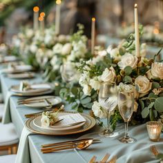 the table is set with silverware and white flowers, gold place settings and candles