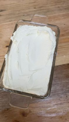 a square cake pan filled with white frosting on top of a wooden table next to a knife