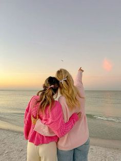 two girls are standing on the beach with their arms around each other and looking at the ocean