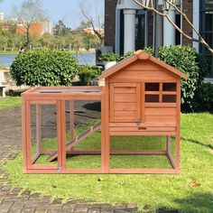 a small wooden chicken coop in front of a large brick building with grass and bushes