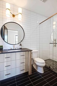 a bathroom with black and white tile flooring, a round mirror above the sink