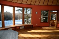 the sun shines through three large windows into a room with wood flooring and red walls