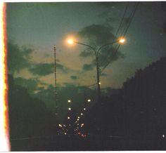 the street lights shine brightly at night in the dark sky, with clouds and trees on either side