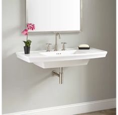 a white sink sitting under a mirror next to a vase with pink flowers in it