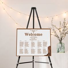 a welcome sign sitting on top of a easel next to a vase with flowers