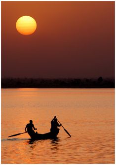 two people on a boat in the middle of water at sunset, with the sun setting behind them