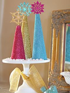 three small christmas trees sitting on top of a white cake stand next to a mirror