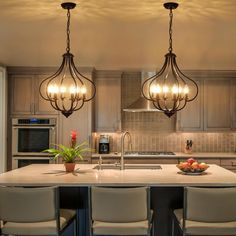 a kitchen island with four lights hanging from it's ceiling and chairs around it