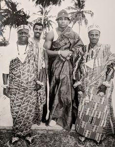 an old black and white photo of four people standing next to each other with palm trees in the background