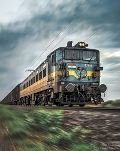 a train traveling down tracks next to a lush green field under a cloudy blue sky