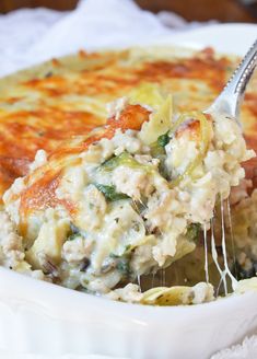 a close up of a casserole dish with a spoon in it and cheese on top