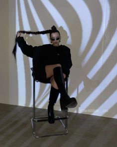 a woman sitting on top of a chair with her hair in a bun and sunglasses